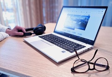 Lächelnde Frau vor ihrem Laptop mit Fensterscheiben im Hintergrund.